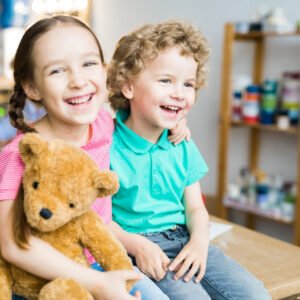 Warm toned portrait of two cute little kids laughing happily and hugging teddy bear toy, copy space